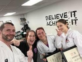 Group of 4 karate students and training smiling with thumbs up and huddled together
